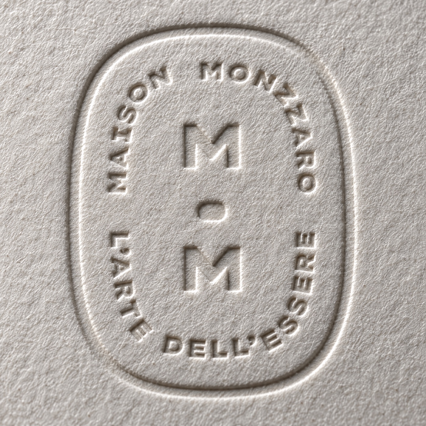 Close macro: the debossed house seal pressed into mono-cotton, raking light, no product